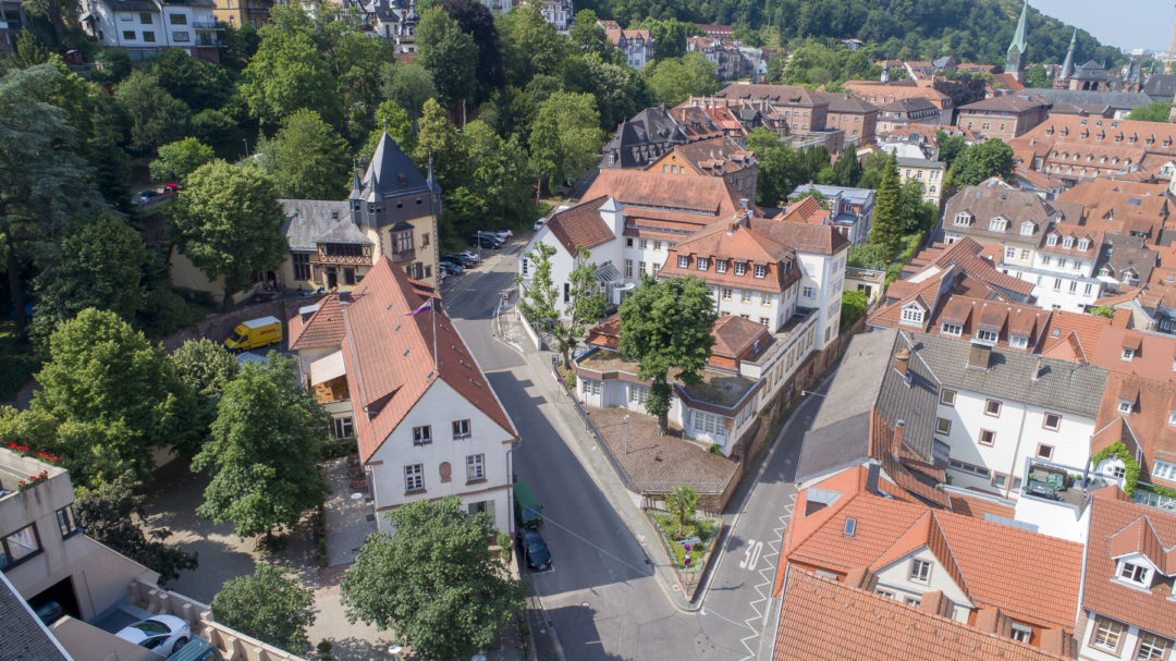 Aerial view of the Documentation and Cultural Center of German Sinti and Roma in Heidelberg. The building is located on a site tapering towards the viewer. On the right, blocks of buildings can be seen in the alleys of Heidelberg's old town, on the left and in the background are individual free-standing buildings.