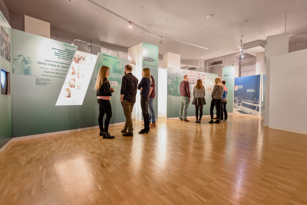 Die Ständige Ausstellung zum Holocaust an den Sinti und Roma in Heidelberg. Zwei Gruppen von Besucherinnen und Besuchern in der Ausstellung.