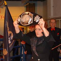 Eine Frau hält einen Meistergürtel aus dem Boxsport mit beiden Händen in die Höhe.