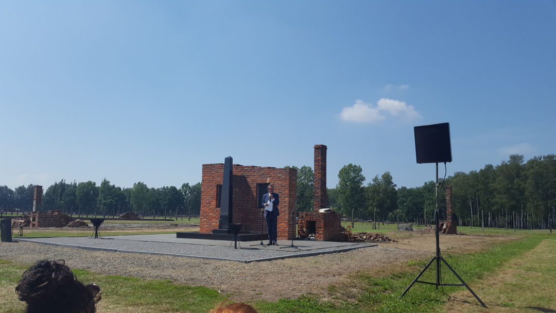 Das Denkmal für die ermordeten Sinti und Roma in Auschwitz-Birkenau. Es ist ein großer Block aus gemauerten Ziegelsteinen. In der Mitte vor dem Block steht eine schwarze Stele.