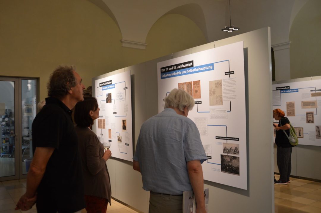 Besucherinnen und Besucher der Ausstellungseröffnung betrachten Ausstellungstafeln.