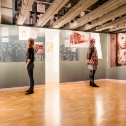 Die Ständige Ausstellung zum Holocaust an den Sinti und Roma in Heidelberg. Zwei Besucherinnen stehen in einem Teil der Ausstellung und lesen.
