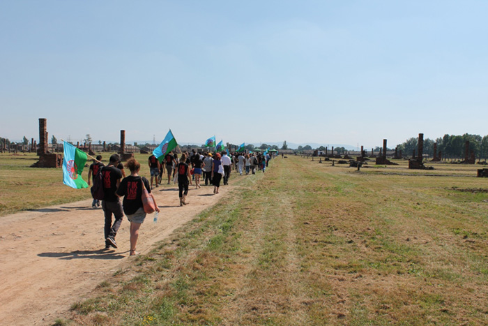 Teilnehmerinnen und Teilnehmer laufen während einer Gedenkveranstaltung in Auschwitz-Birkenau auf einem Schotterweg.