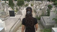 Eine Frau läuft einen Weg auf einem Friedhof entlang. Links und rechts von ihr sind zahlreiche Gräber zu sehen.