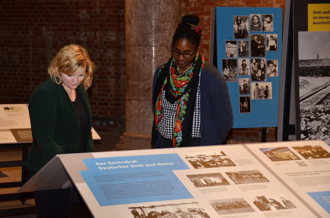 Zwei Besucherinnen stehen in der Ausstellung an einem Tisch mit einer Ausstellungstafeln und lesen aufmerksam die Texte.