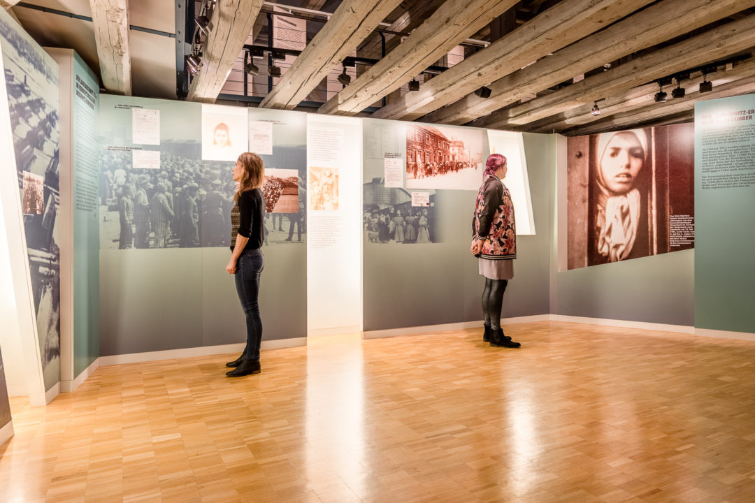 Blick in die Dauerausstellung des Dokumentations- und Kulturzentrums. Zwei Besucherinnen stehen vor großen Ausstellungstafeln und lesen.