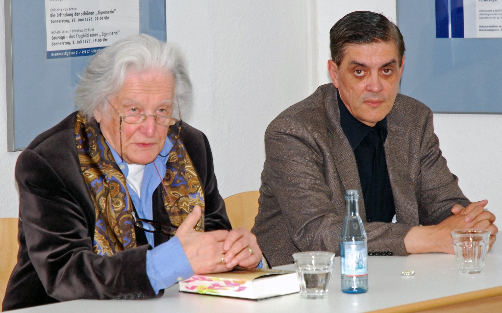 Ralph Giordano (links) und Romani Rose (rechts) bei einer Lesung im Dokumentations- und Kulturzentrum an einem Tisch auf dem Podium. Ralph Giordano spricht.