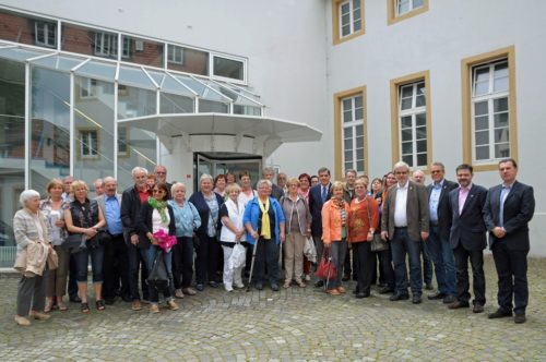 Die Delegation aus Mörfelden-Walldorf steht mit Mitarbeiterinnen und Mitarbeitern des Dokumentationszentrums für ein Gruppenbild im Innenhof des Zentrums. Im Hintergrudn ist der gläserne Eingangsbereich zu sehen.