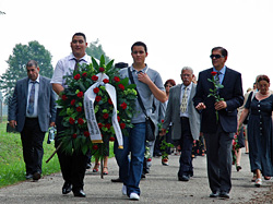 Zwei Jugendliche tragen einen Trauerkranz. Hinter ihnen laufen weitere Teilnehmerinnen und Teilnehmer der Reise.