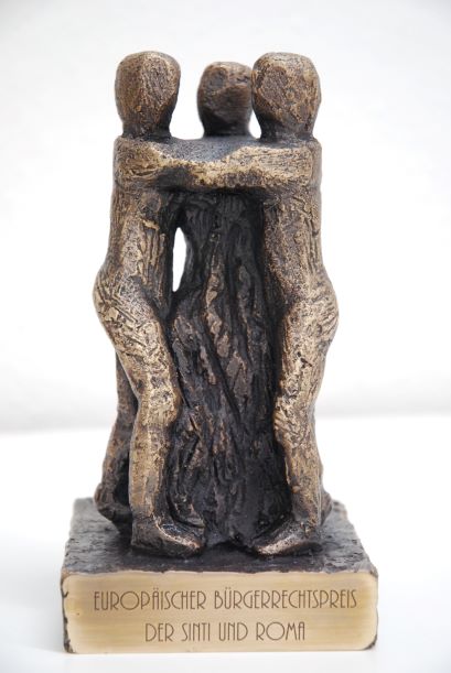 Die Skulptur des Europäischen Bürgerrechtspreises aus gegossener Bronze. Drei abstrakte menschliche Figuren halten sich an den Schultern gefasst.