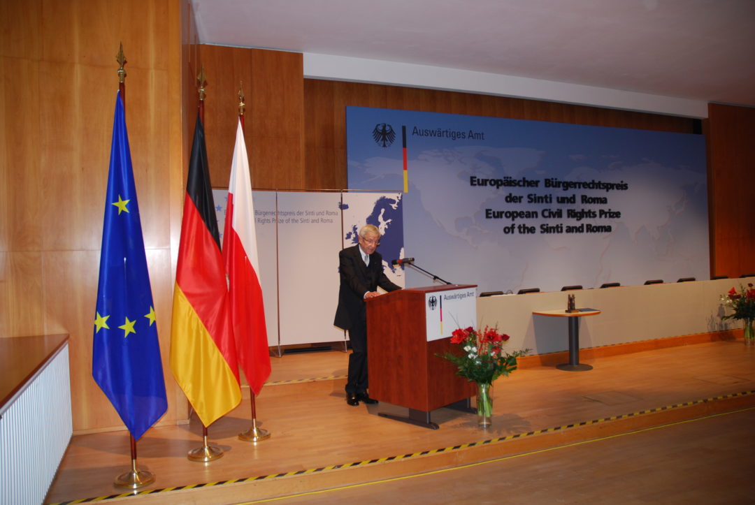 Manfred Lautenschläger im Auswärtigen Amt während seiner Rede. Er steht an einem Rednerpult, links neben ihm stehen die europäische, die deutsche und die polnische Flagge. Rechts neben ihm ist der Titel der Veranstaltung auf einer großen Leinwand angebracht.