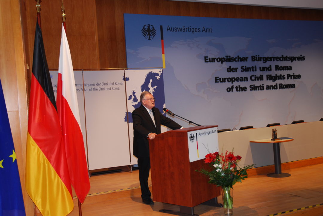 Erwin Teufel im Auswärtigen Amt während seiner Rede. Er steht an einem Rednerpult, links neben ihm stehen die europäische, die deutsche und die polnische Flagge. Rechts neben ihm ist der Titel der Veranstaltung auf einer großen Leinwand angebracht.