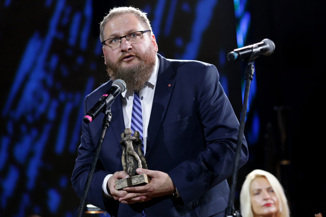 Verleihung des Sonderpreises des Europäischen Bürgerrechtspreises 2019 an Piotr Cywiński. Der Preisträger steht während seiner Dankesrede vor einem Mikrofon. In seinen Händen hält er die Skulptur des Bürgerrechtspreises.