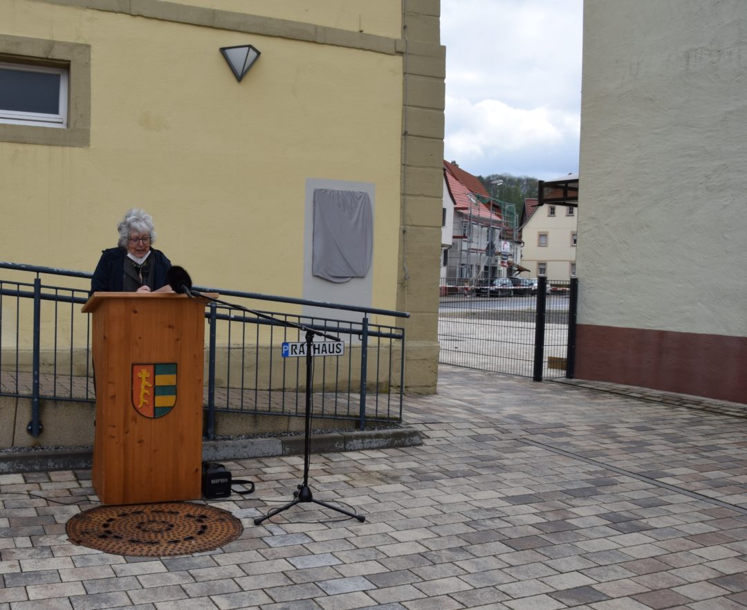 Elsbeth Wagner steht an einem Rednerpult vor der Gedenktafel in Hoffenheim.