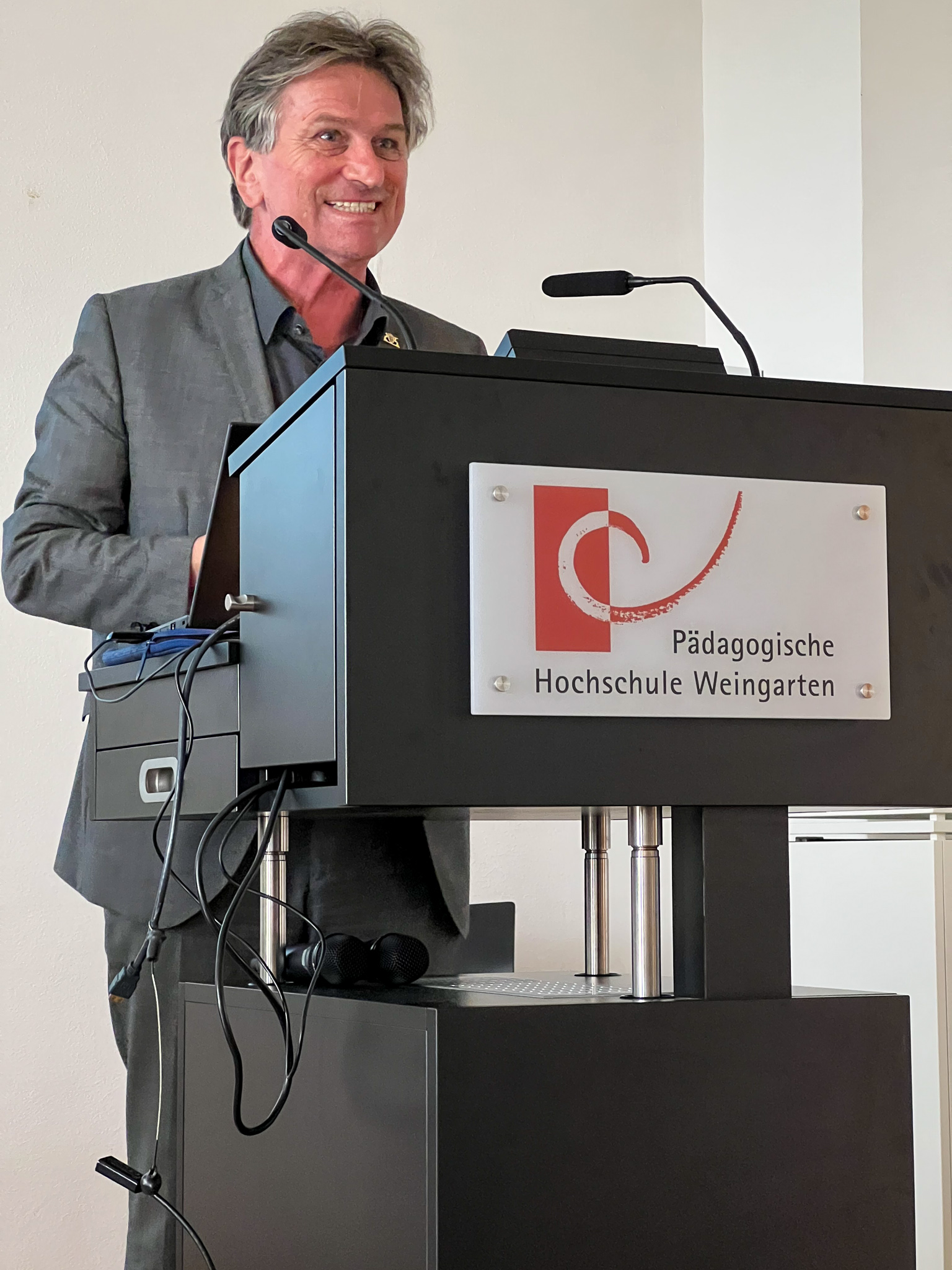 Manfred Lucha, Minister für Soziales, Gesundheit und Integration Baden-Württemberg, bei der Ausstellungseröffnung an einem Pult der Pädagogischen Hochschule Weingarten..
