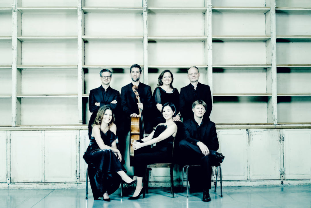 Sieben Mitglieder des Alban Berg Ensemble Wien. Drei Mitglieder sitzen auf Stühlen, dahiner stehen vier weitere Mitglieder. Einer hält ein Cello.
