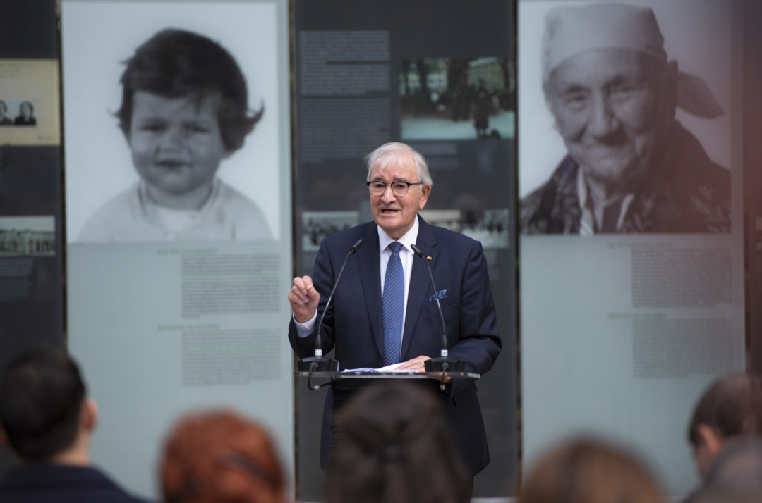 Dutch Holocaust survivor Zoni Weisz stands at a lectern. Behind him is an open-air exhibition with information on the individual fates of Sinti and Roma persecuted under National Socialism.