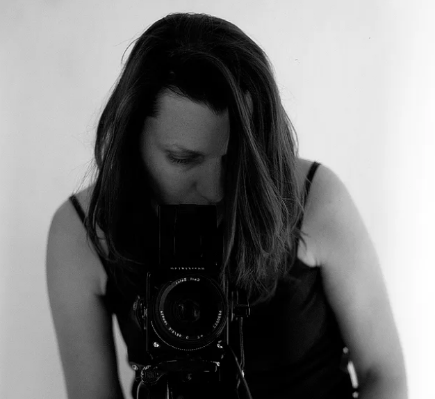 Valérie Leray blick in eine Fotokamera. Die Kamera ist zum Betrachter/zur Betrachterin hin ausgerichtet.