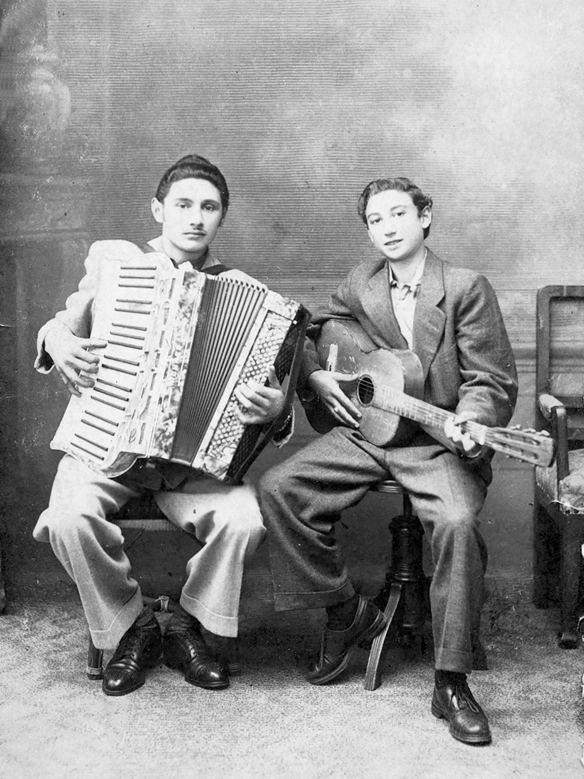 Mirano Cavaljeti-Richter (rechts) und sein Bruder Harry (links) sitzen nebeneinander auf Stühlen. Mirano hält eine Gitarre, Harry ein Akkordeon.