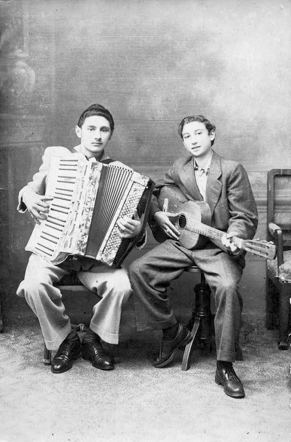 Mirano Cavaljeti-Richter (rechts) und sein Bruder Harry (links) sitzen nebeneinander auf Stühlen. Mirano hält eine Gitarre, Harry ein Akkordeon.
