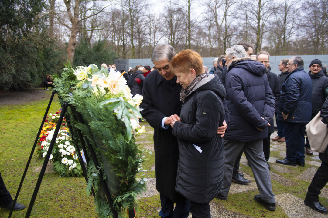 Romani Rose und die Bundestagsvizepräsidentin Petra Pau stehen zusammen vor einem Gedenkkranz und halten sich an der Hand.