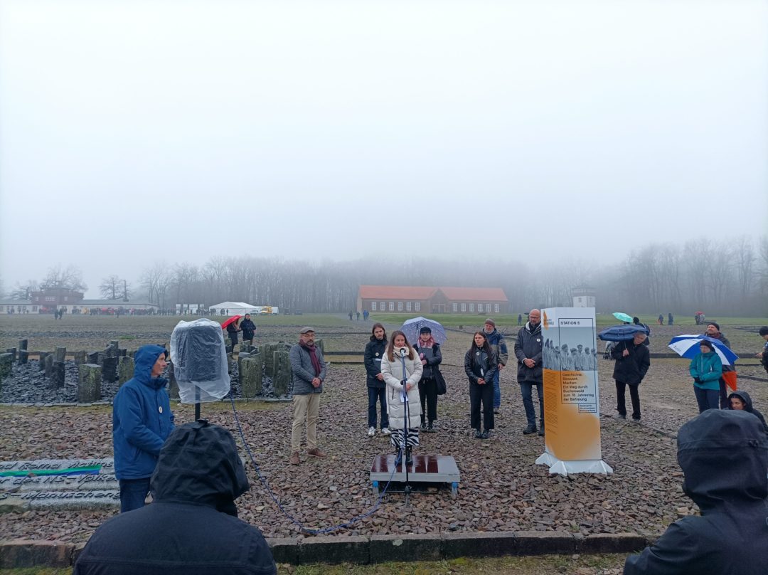 Melody Steinbach speaks into a microphone on the grounds of the Buchenwald concentration camp memorial.