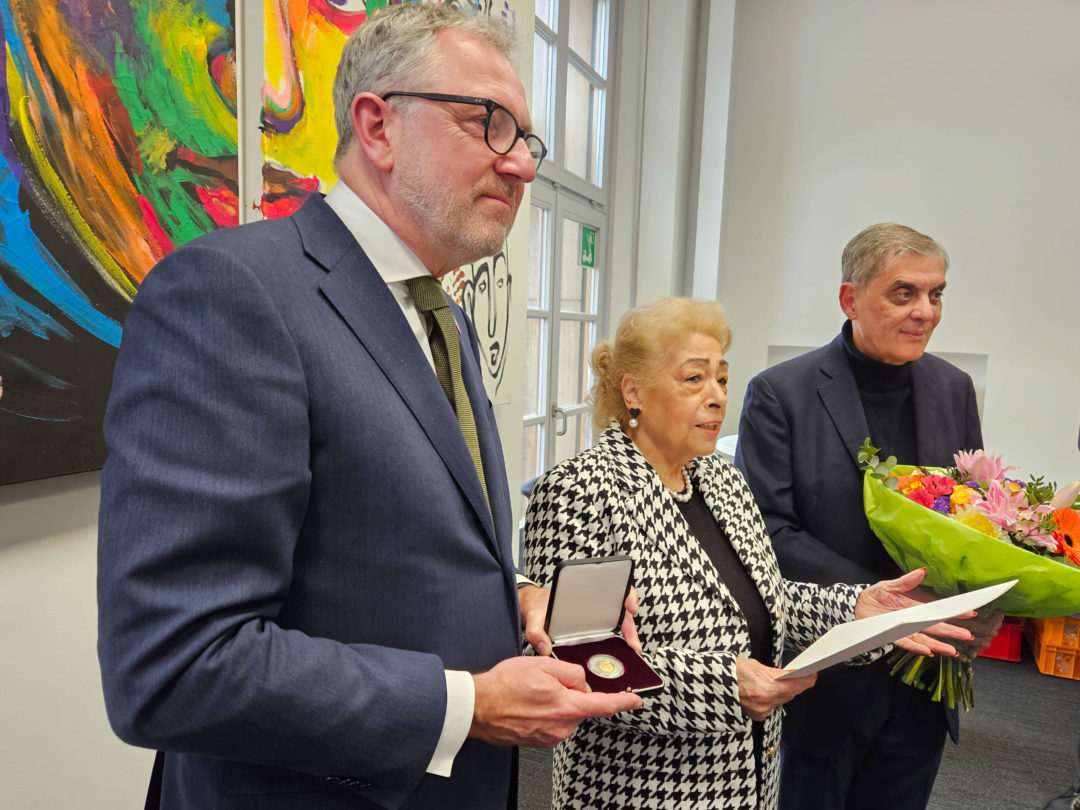 Der Mannheimer Oberbürgermeister Peter Kurz hält eine Schatulle mit der goldenen Staufermedaille in der Hand. Neben ihm steht Ilona Lagrene während ihrer Dankesrede. Ganz rechts steht Romani Rose mit einem Blumenstrauß.