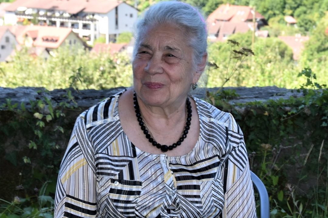Raisa Nabaranchuk is sitting in a garden overlooking a valley. To her left and right sit her sisters.