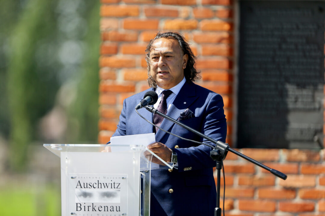 Roman Kwiatkowski stands in front of a microphone at a lectern and gives a speech at the site of the former Auschwitz-Birkenau death camp.