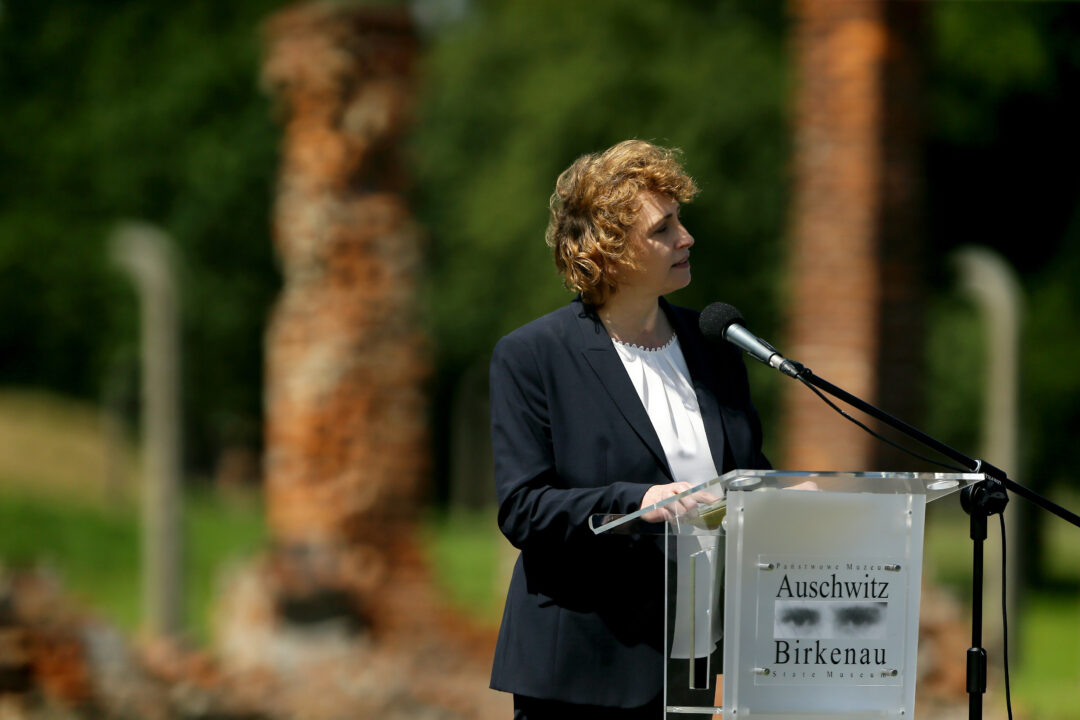 Nicola Beer stands in front of a microphone at a lectern and gives a speech at the site of the former Auschwitz-Birkenau death camp.